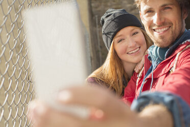 Couple taking self-portrait with camera phone next to chain link fence - CAIF17665