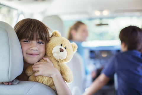 Portrait of happy girl with teddy bear in back seat of car stock photo