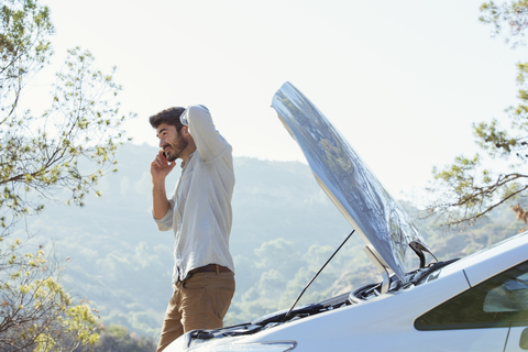 Man talking on cell phone with automobile hood raised at roadside stock photo