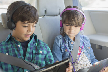 Bruder und Schwester mit Kopfhörern und digitalen Tablets auf dem Rücksitz eines Autos - CAIF17688