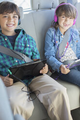 Porträt eines glücklichen Geschwisterpaares mit Kopfhörern und digitalen Tablets auf dem Rücksitz eines Autos - CAIF17690
