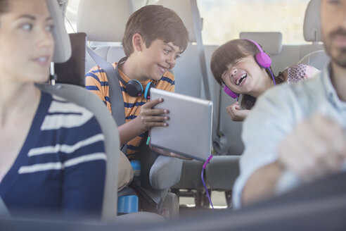 Glückliche Geschwister, die ein digitales Tablet auf dem Rücksitz eines Autos benutzen - CAIF17692