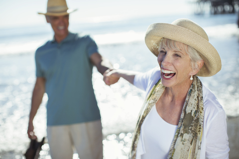 Begeistertes älteres Paar hält sich am sonnigen Strand an den Händen, lizenzfreies Stockfoto