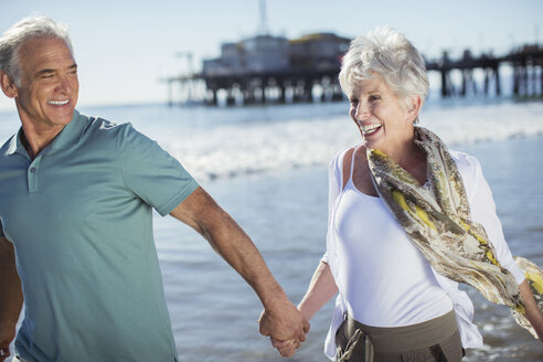 Begeistertes Seniorenpaar beim Laufen am Strand - CAIF17746