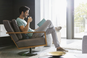 Mann trinkt Tee und liest ein Buch im Wohnzimmer - CAIF17878