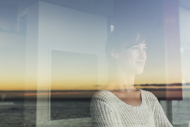 Woman overlooking sunset and ocean from window - CAIF17932