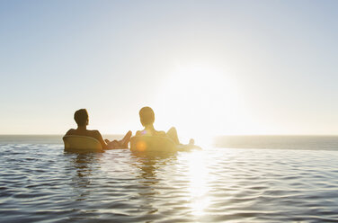 Paar in Liegestühlen im Infinity-Pool mit Blick auf das Meer - CAIF17935