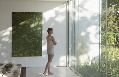 Frau steht am Fenster in einem modernen Schlafzimmer - CAIF17972