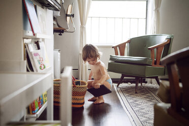 Girl crouching while holding book at home - CAVF09161