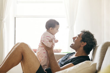 Seitenansicht des Vaters, der mit seiner Tochter spielt, während er zu Hause auf dem Sofa sitzt - CAVF09166