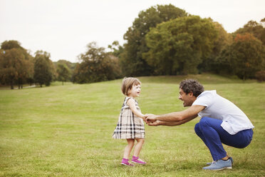 Seitenansicht des Vaters, der im Park hockt und die Hände seiner Tochter hält - CAVF09227