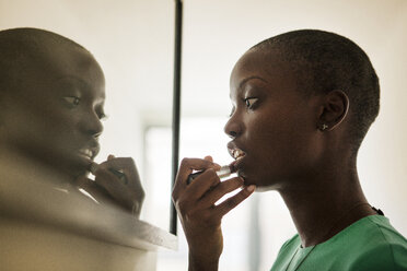 Side view of woman applying lipstick while standing by mirror at home - CAVF09241