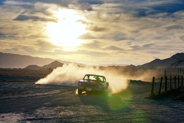 Mann fährt Auto auf einem Feld bei Sonnenuntergang - CAVF09361