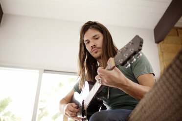 Niedriger Blickwinkel eines Mannes, der Gitarre spielt, während er zu Hause auf dem Sofa sitzt - CAVF09378