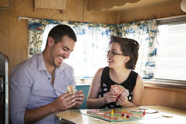 Happy couple playing board game while sitting in camper van - CAVF09405