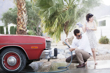 Mann bespritzt Frau beim Autowaschen auf dem Parkplatz mit Wasser - CAVF09419
