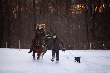 Mann hält Seil, während Frau auf Pferd auf verschneitem Feld reitet - CAVF09492