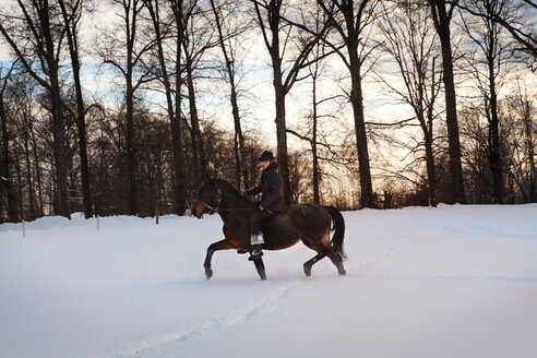 Mann reitet Pferd auf verschneitem Feld - CAVF09493