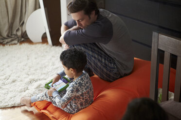 Boy using tablet while sitting with father at home - CAVF09522