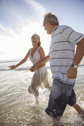 Older couple playing in waves on beach - CAIF18065