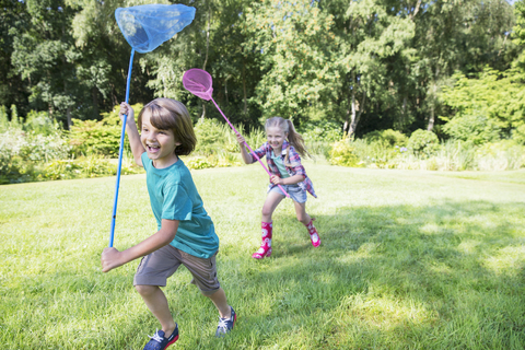 Junge und Mädchen laufen mit Schmetterlingsnetzen im Gras, lizenzfreies Stockfoto