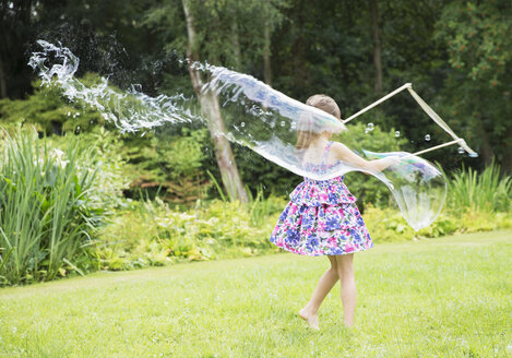 Girl making large bubbles in backyard - CAIF18113