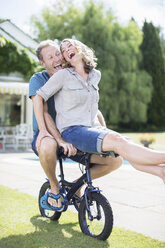 Couple riding small bicycle in grass - CAIF18116