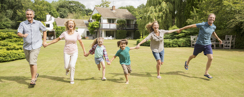 Mehrgenerationenfamilie, die sich an den Händen hält und im Gras läuft, lizenzfreies Stockfoto