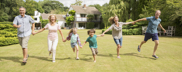 Multi-generation family holding hands and running in grass - CAIF18118