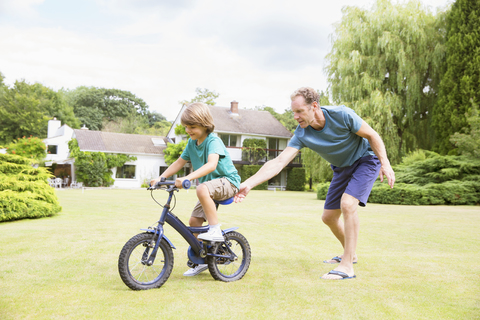 Vater schiebt Sohn auf dem Fahrrad im Hinterhof, lizenzfreies Stockfoto