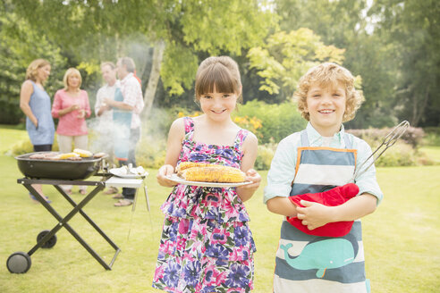 Bruder und Schwester halten gegrillten Mais in der Nähe des Grills im Hinterhof - CAIF18128