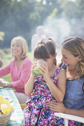 Girl drinking juice on mother's lap in backyard - CAIF18139