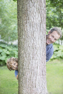 Vater und Sohn spähen hinter einem Baum hervor - CAIF18149