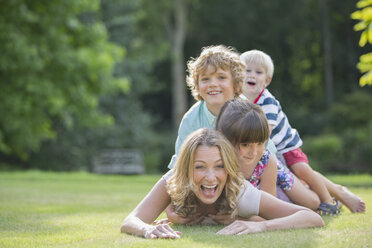 Children laying on mother in grass - CAIF18151