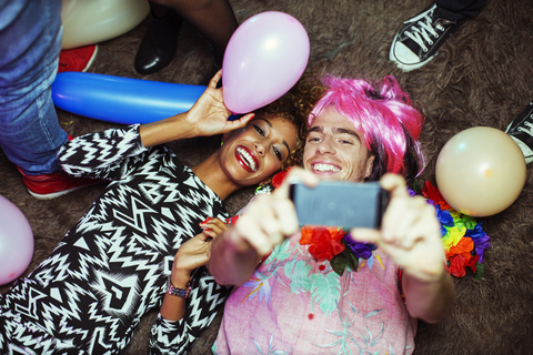 Paar nimmt Selbstporträt mit Handy auf dem Boden bei Party, lizenzfreies Stockfoto
