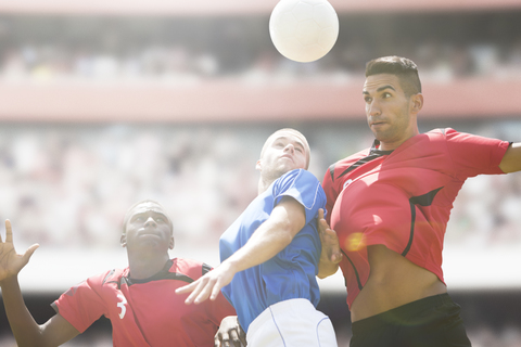 Fußballspieler springen auf dem Spielfeld um den Ball, lizenzfreies Stockfoto