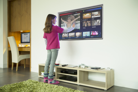 Mädchen mit Touchscreen-Fernseher im Wohnzimmer, lizenzfreies Stockfoto