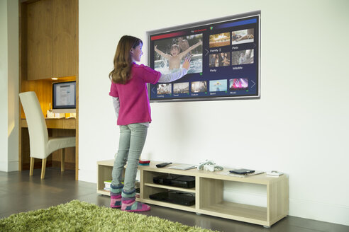 Mädchen mit Touchscreen-Fernseher im Wohnzimmer - CAIF18430