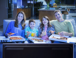 Familie isst Pizza vor dem Fernseher im Wohnzimmer - CAIF18435