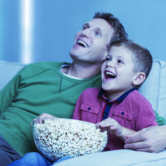 Vater und Sohn sehen auf dem Sofa fern - CAIF18438