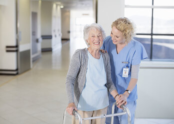 Nurse helping senior patient with walker in hospital corridor - CAIF18495