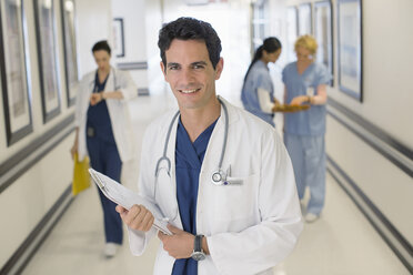Porträt eines lächelnden Arztes im Krankenhauskorridor - CAIF18503