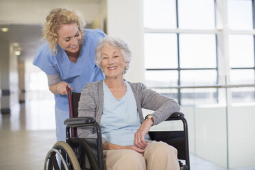 Krankenschwester und älterer Patient lächelnd im Krankenhausflur - CAIF18504