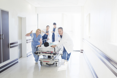 Ärzte und Krankenschwestern hetzen einen Patienten auf einer Bahre den Krankenhausflur hinunter, lizenzfreies Stockfoto