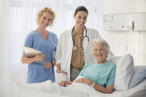 Arzt, Krankenschwester und älterer Patient lächelnd im Krankenhauszimmer, lizenzfreies Stockfoto
