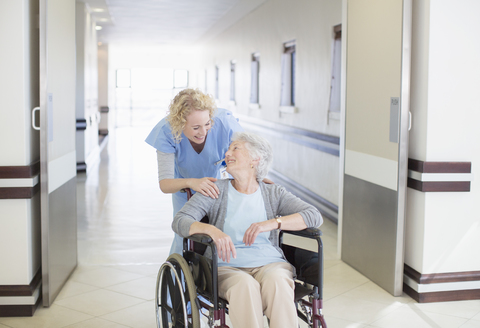 Krankenschwester mit älterem Patienten im Rollstuhl auf dem Krankenhausflur, lizenzfreies Stockfoto