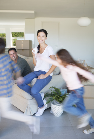 Eltern beobachten Kinder, die im Wohnzimmer eines neuen Hauses herumlaufen, lizenzfreies Stockfoto