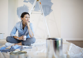 Woman relaxing with coffee among painting supplies - CAIF18557