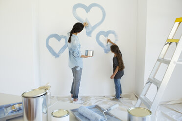 Mother and daughter painting blue hearts on wall in new house - CAIF18559