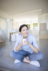 Happy woman enjoying coffee among cardboard boxes - CAIF18561